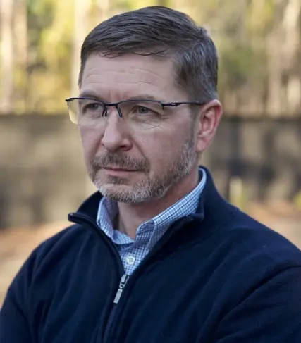 A man with glasses and a beard wearing a blue jacket.