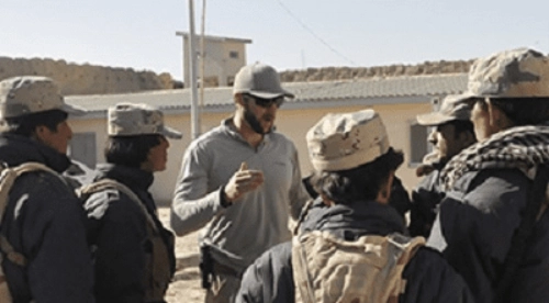 A man in grey shirt and hat talking to people.